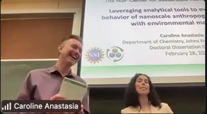screen shot of zoom view labeled "Caroline Anastasia," showing two smiling people standing in front of a powerpoint slide